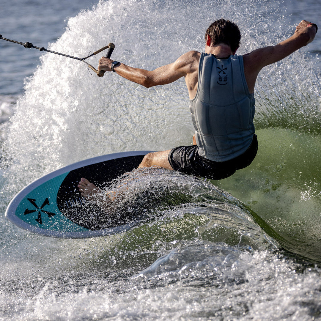 A person riding the 2026 Phase Five Avenger wakesurf board, carving through a wave with spray flying around.