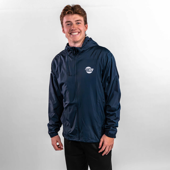 A young man wearing a navy offshore jacket with a logo, smiling against a light background.