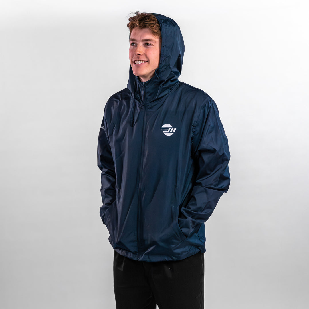 A young man wearing a navy offshore jacket with a hood, smiling against a neutral background.