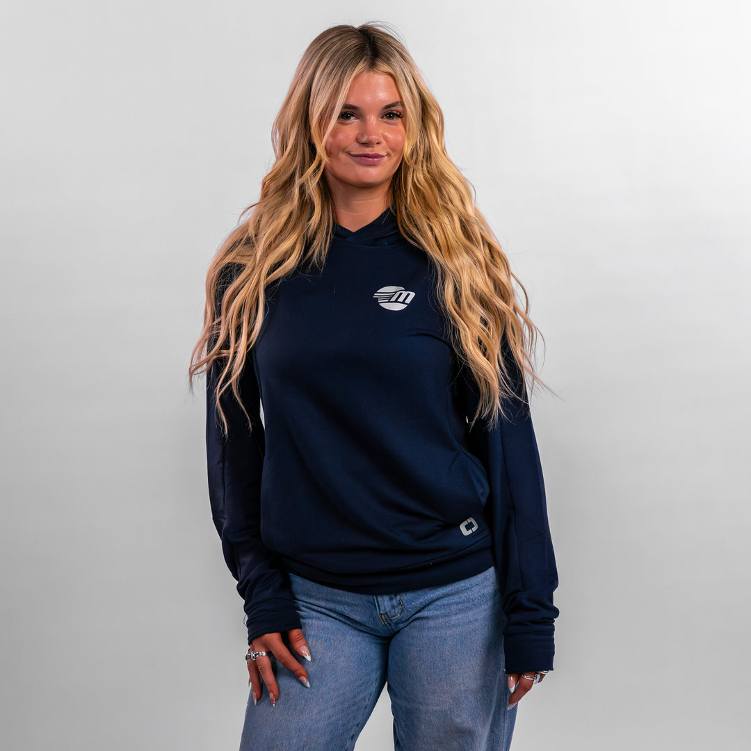 Model wearing a navy Malibu Performance Hoodie with a logo, paired with light blue jeans, showcasing a casual style.