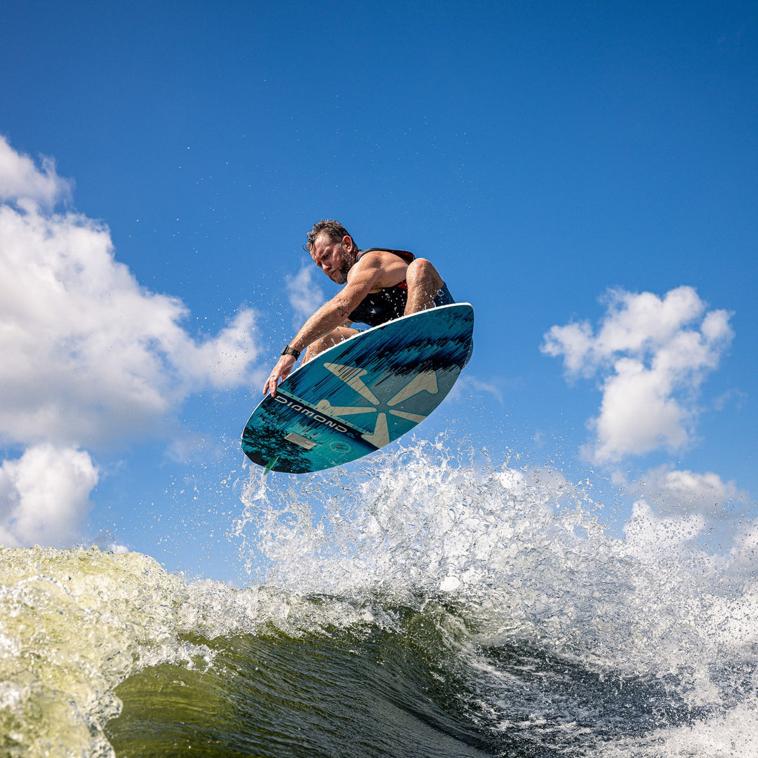 A person performing a jump on a 2026 Phase Five Diamond CL surfboard over a wave, showcasing dynamic water sports action.
