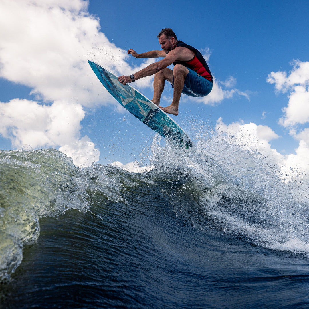 A person performs a jump on a 2026 Phase Five Diamond CL surfboard over a wave, showcasing water sports action.