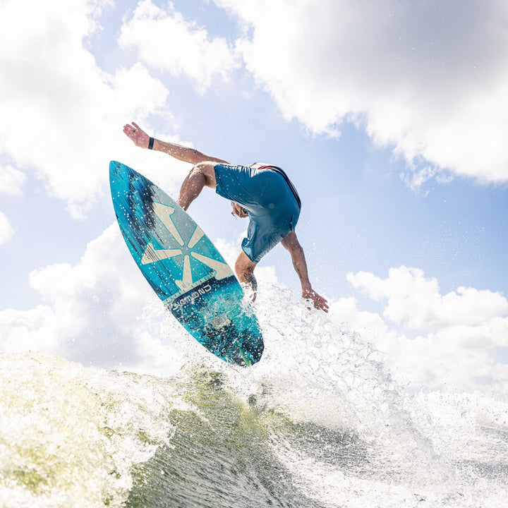 A surfer performs a jump on the 2026 Phase Five Diamond CL wake surfboard, creating a splash in the water.