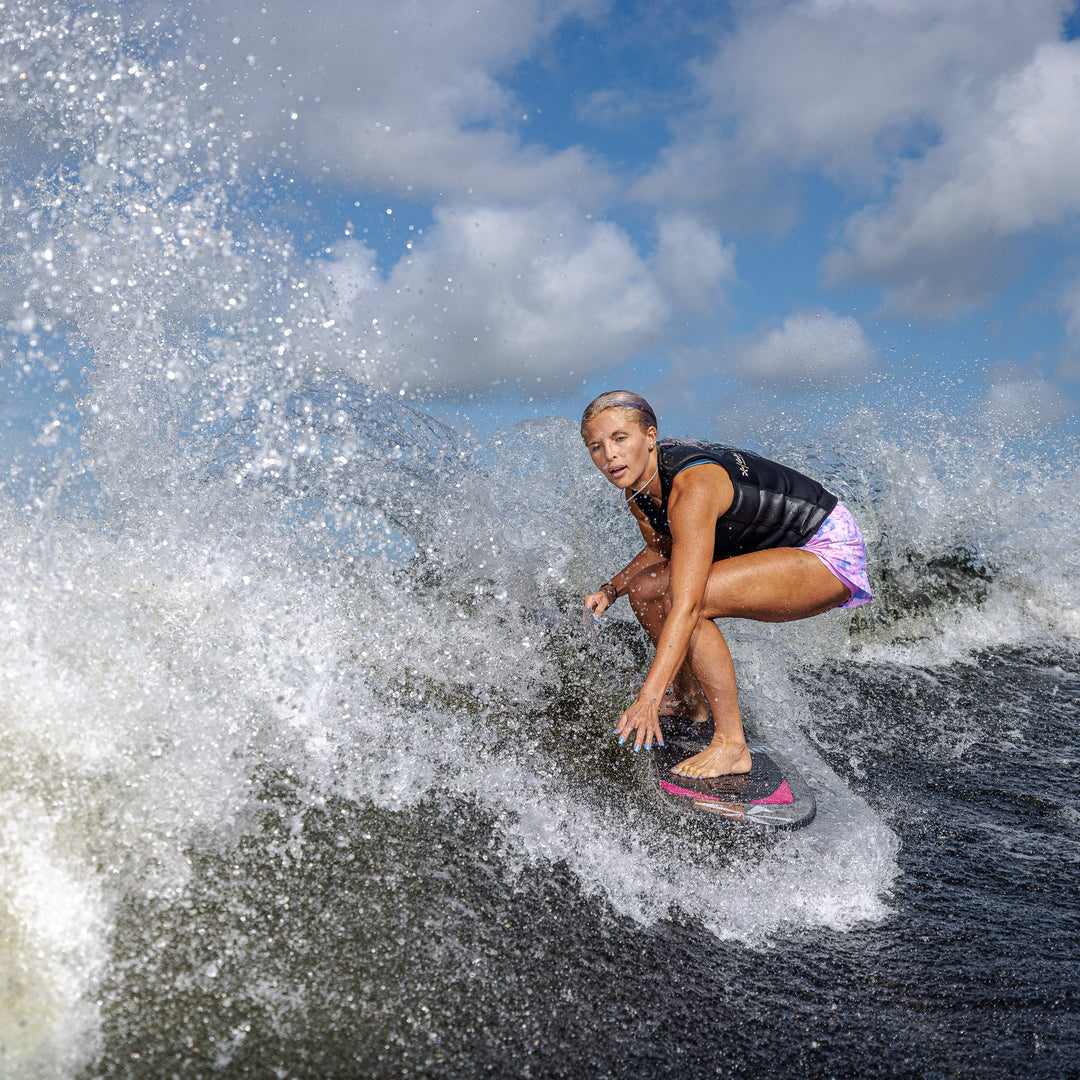 A woman rides a surfboard on a wave, showcasing the 2026 Phase Five Diamond Luv in action.