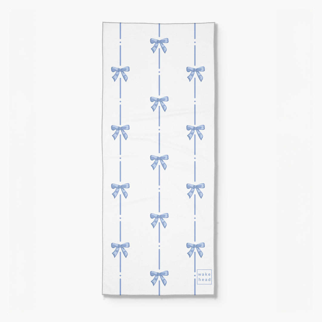Blue and white towel with a pattern of bows and dashed lines, labeled "Wake Head - Blue Bliss Lake Towel".