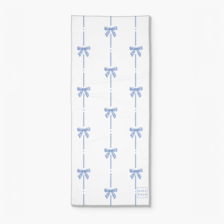 Blue and white towel with a pattern of bows and dashed lines, labeled "Wake Head - Blue Bliss Lake Towel".