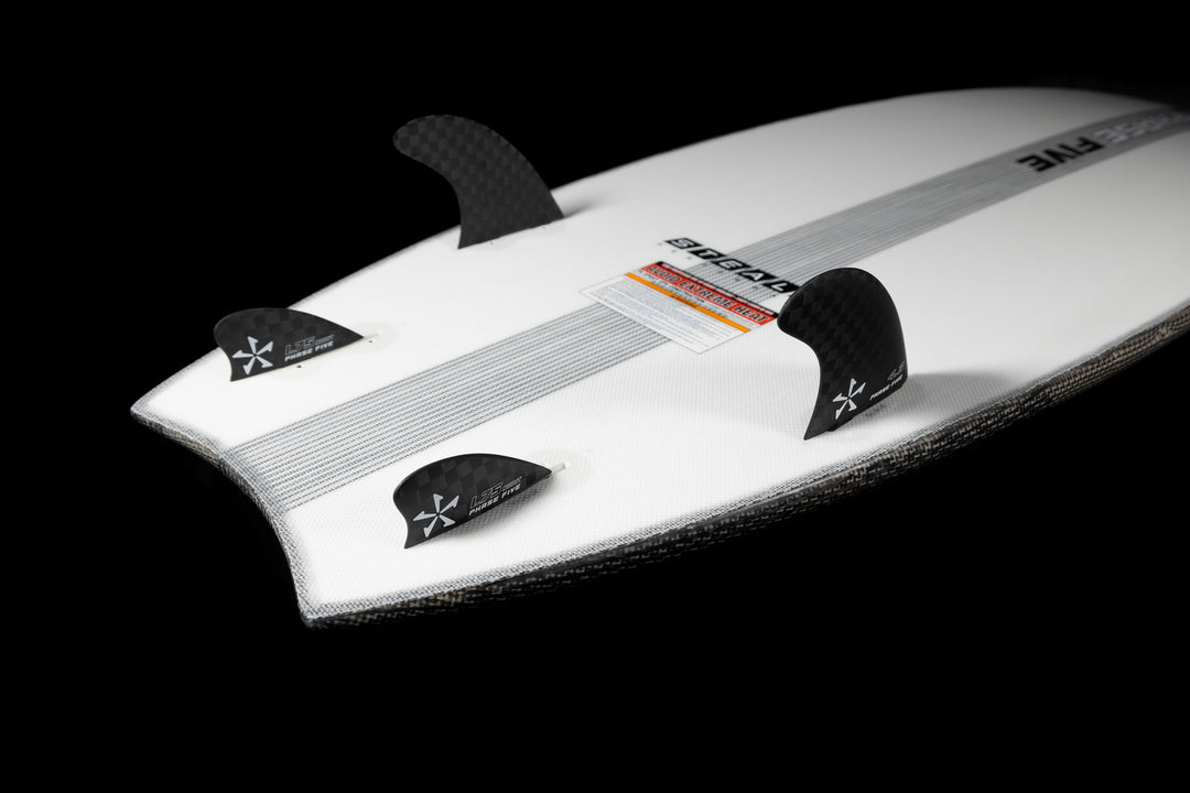 2025 Phase 5 Ahi Stealth surfboard with black carbon fiber fins on a white board against a black background.