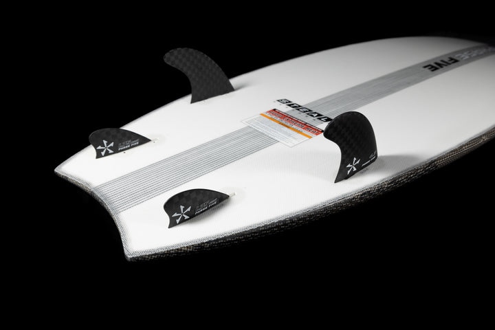 2025 Phase 5 Ahi Stealth surfboard with black carbon fiber fins on a white board against a black background.