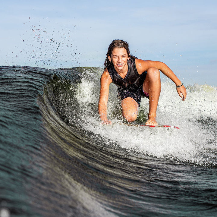 A young girl rides a wave on a 2025 Phase 5 Fish Skim Board, showcasing her skill and excitement on the water.