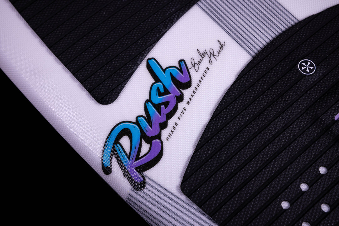 Close-up of the 2025 Phase 5 Rush surfboard featuring a black and white textured design with a colorful "Rush" logo and signature.