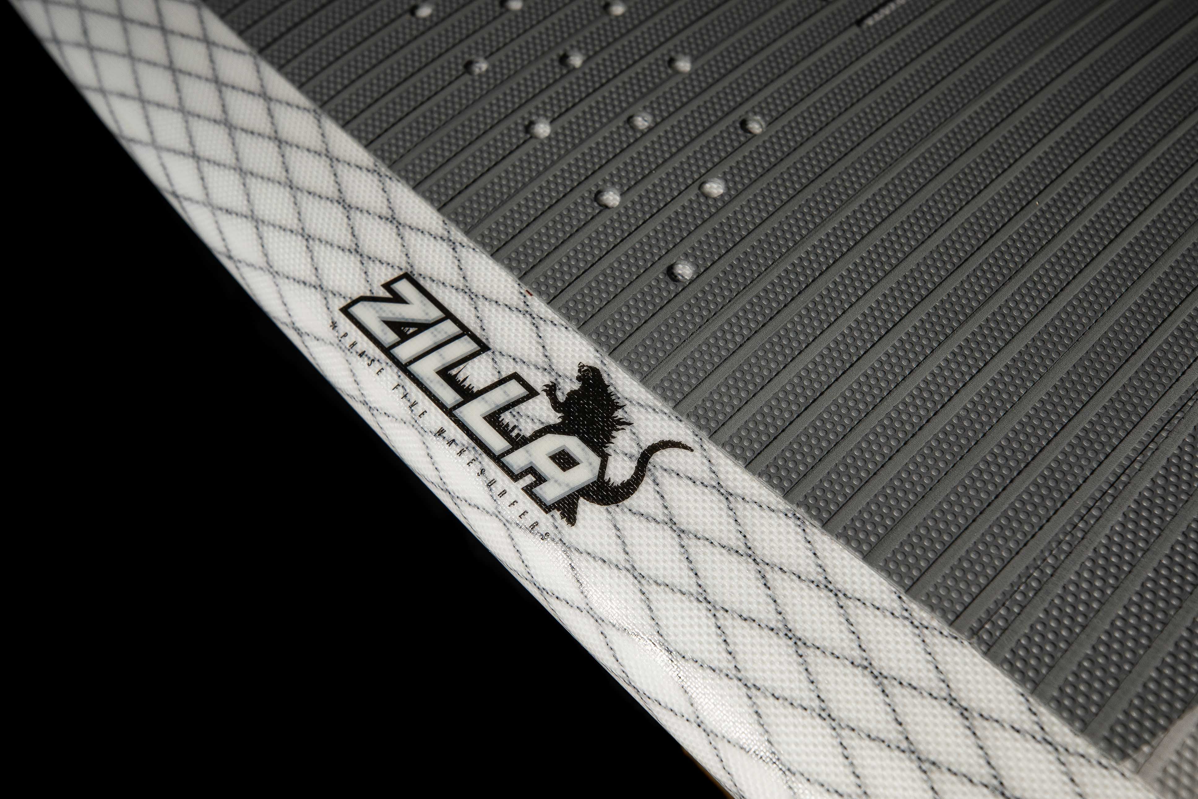 Close-up of the 2025 Phase 5 Zilla Surf Board's textured deck with a white edge and black logo featuring a lizard.