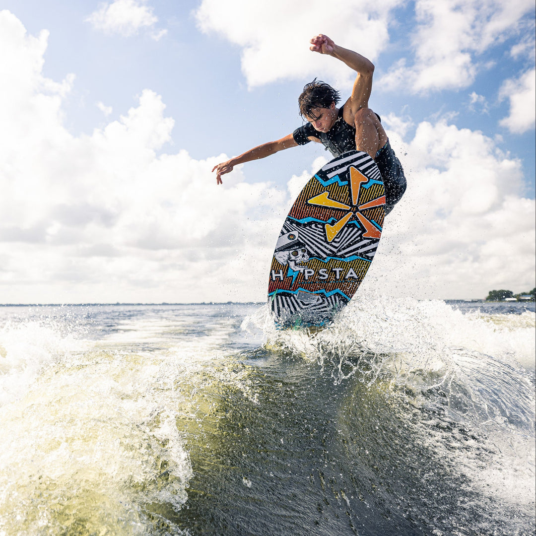 A person performs a jump on a wakeboard over a wave, showcasing the 2026 Phase Five Hypsta V2 design.