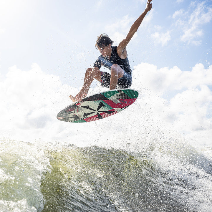 A young man performs a jump on a wakeboard over a wave, showcasing the 2026 Phase Five Key CL design.