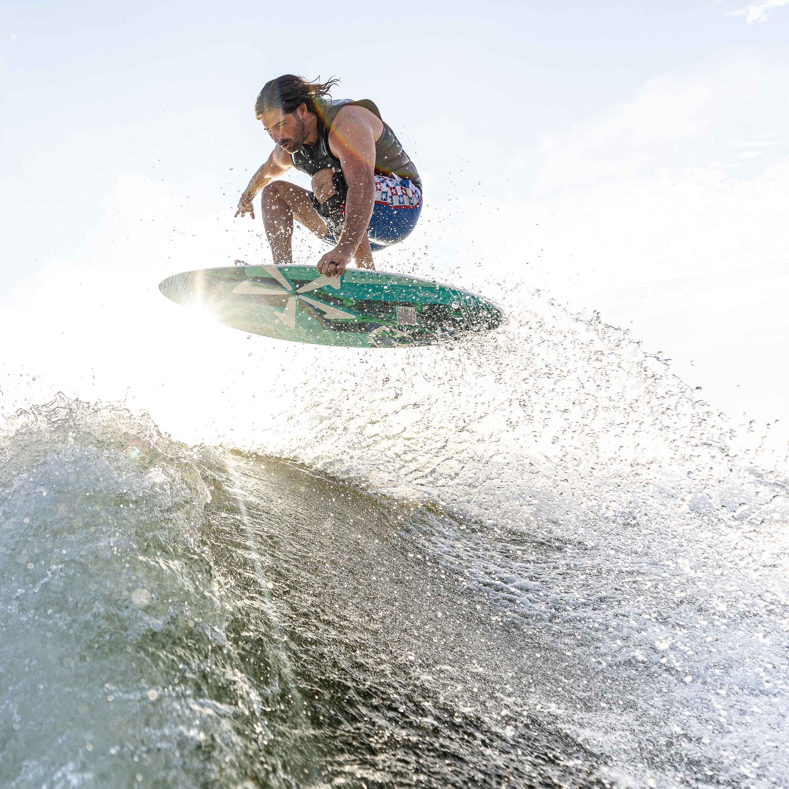 A male surfer jumps over a wave on a 2025 Phase 5 Key CL Skim Board during daytime.