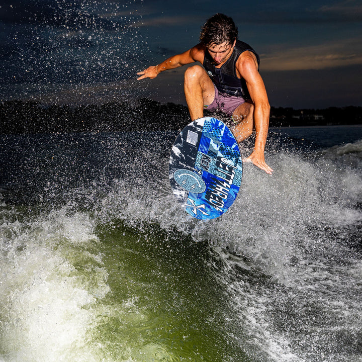 A rider performs an aerial trick on the 2026 Phase Five Key Jett Shreds wake surfboard, creating a splash in the water.
