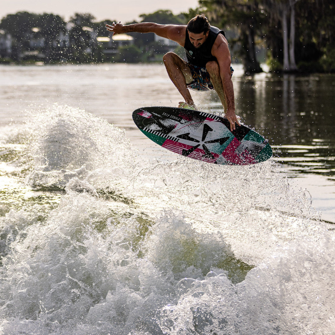 A person performs a jump on a colorful wake surfboard over a wave, showcasing the 2026 Phase Five Key V2 in action.