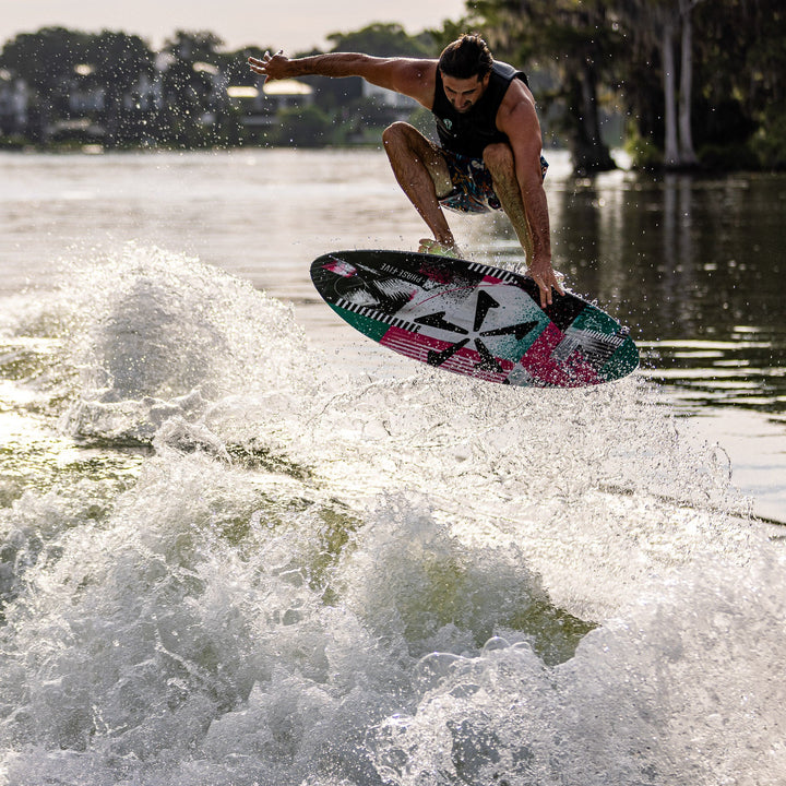 A person performs a jump on a colorful wake surfboard over a wave, showcasing the 2026 Phase Five Key V2 in action.