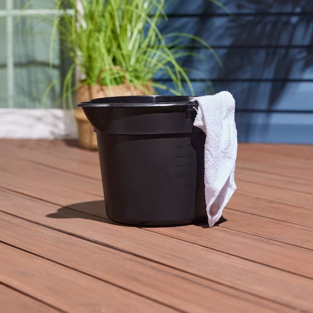 Black detailing bucket with a white towel draped over the side, placed on a wooden deck outdoors.