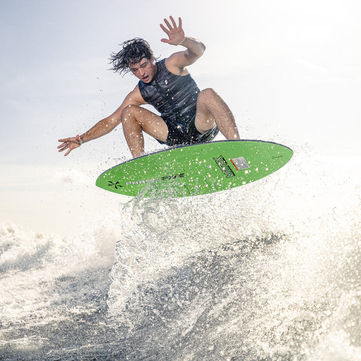 A person performing a jump on a green Phase Five Matrix surfboard, creating a splash in the water.