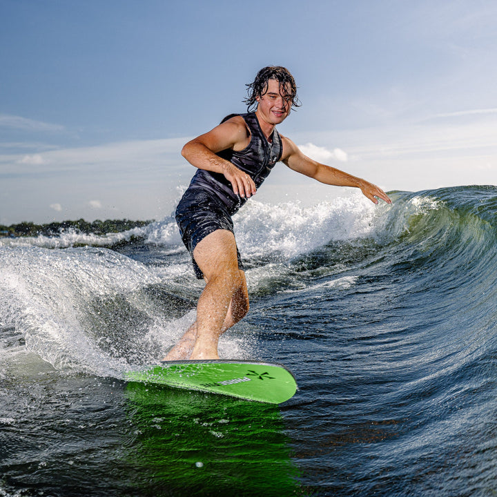 A person surfing on a green Phase Five Matrix board, riding a wave under a clear sky.