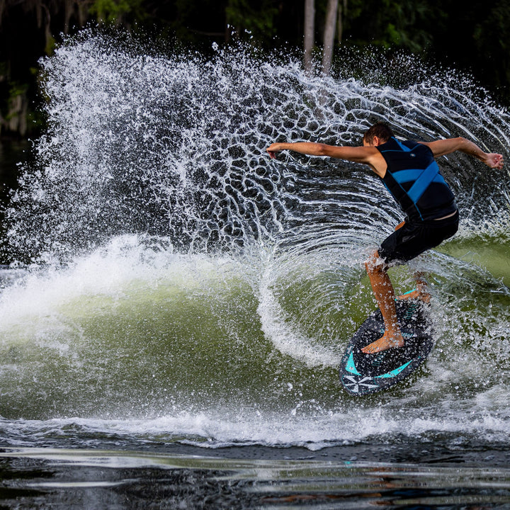 A person performs a trick on the 2026 Phase Five Matrix Pro wakesurf board, creating a spray of water behind them.