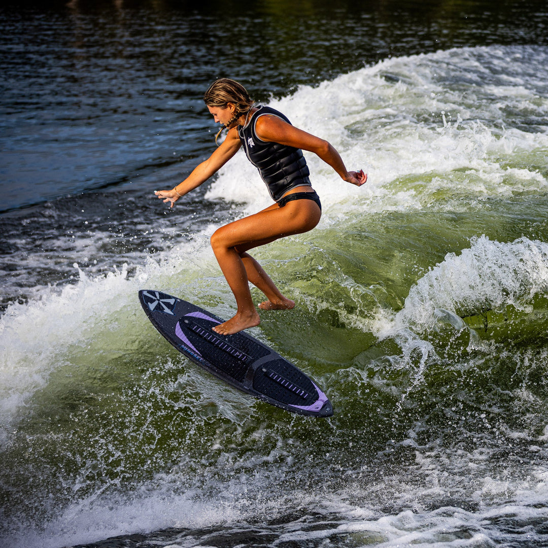 A person surfing on a 2026 Phase Five Mindset board, riding a wave with a dynamic stance and a backdrop of water splashes.