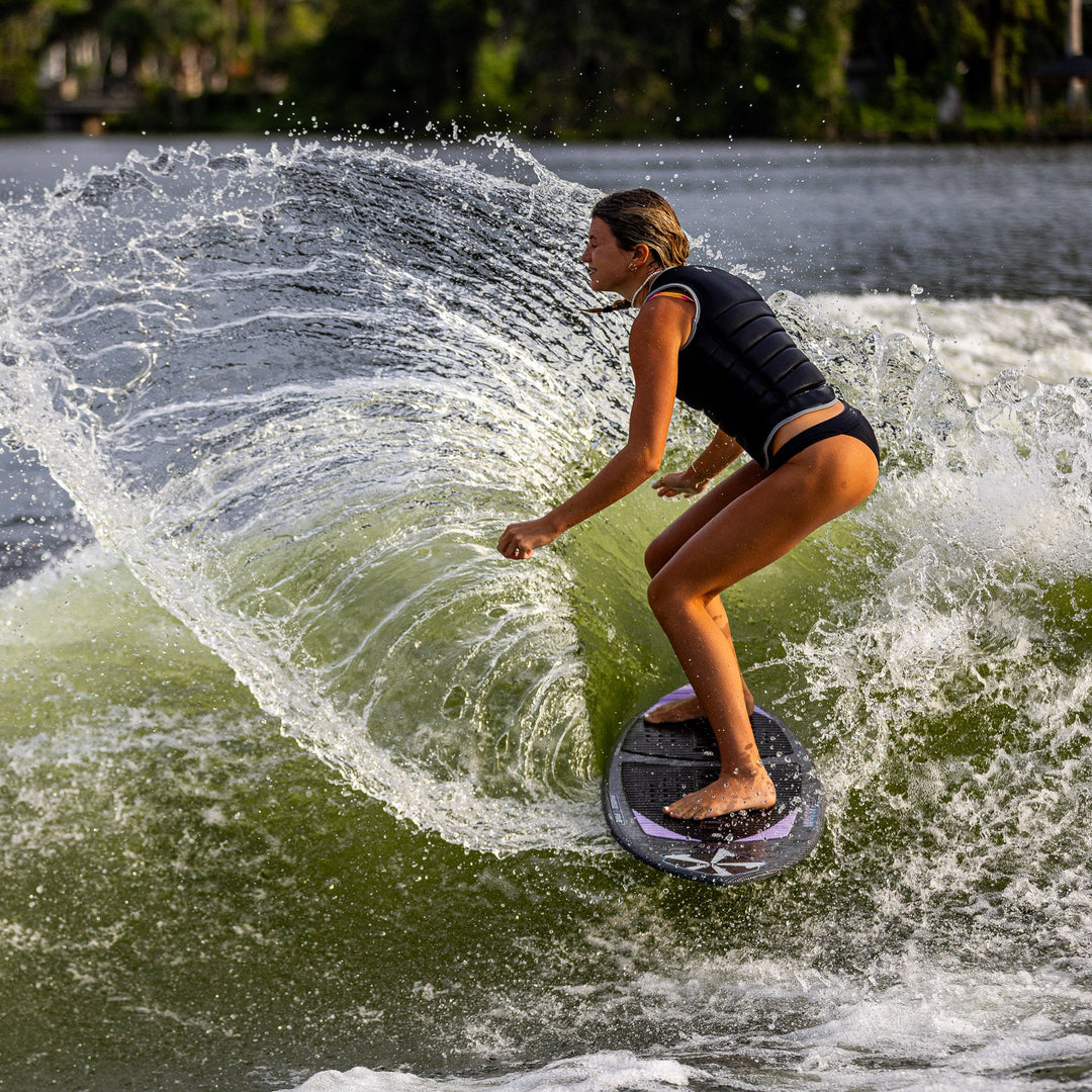 A person riding the 2026 Phase Five Mindset wakesurf board, carving through a wave with spray and sunlight.