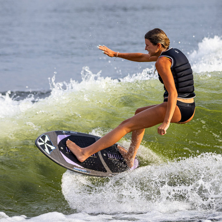 A woman rides the 2026 Phase Five Mindset surfboard, carving through a wave with skill and balance.