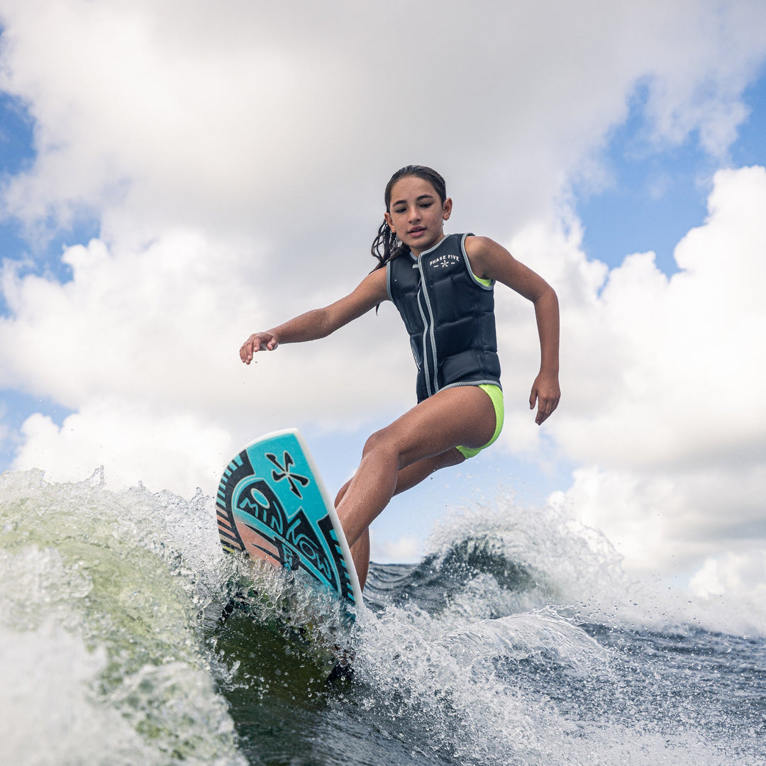 A young girl rides the waves on a 2026 Phase Five Minnow surfboard, showcasing her skills in a life jacket.