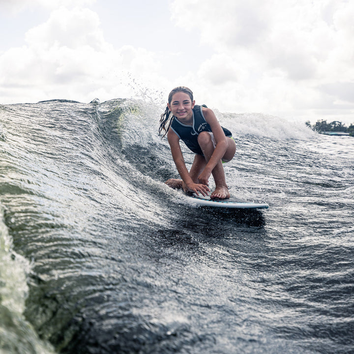 A young girl rides a wave on a surfboard, showcasing the agility and fun of the 2026 Phase Five Minnow.