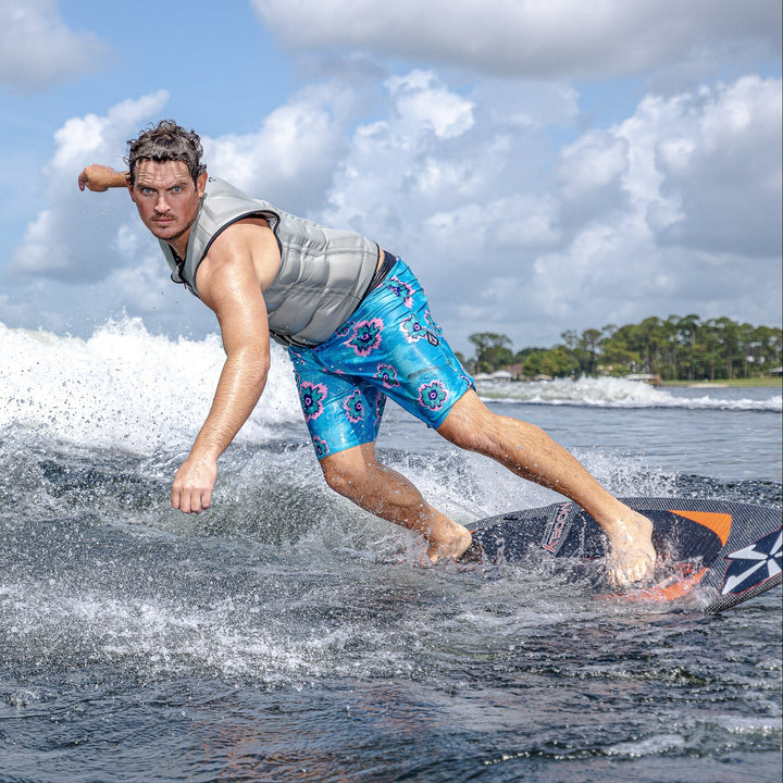 A man rides a surfboard on a wave, showcasing the 2026 Phase Five Model X, with a vibrant background of water and sky.