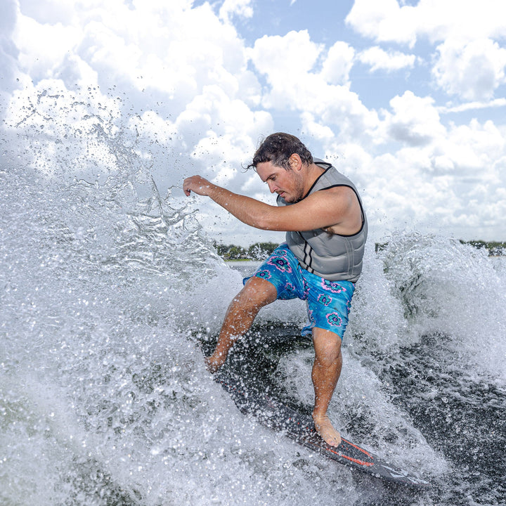 A man in a life vest rides the 2026 Phase Five Model X surfboard on a wave, showcasing dynamic water sports action.