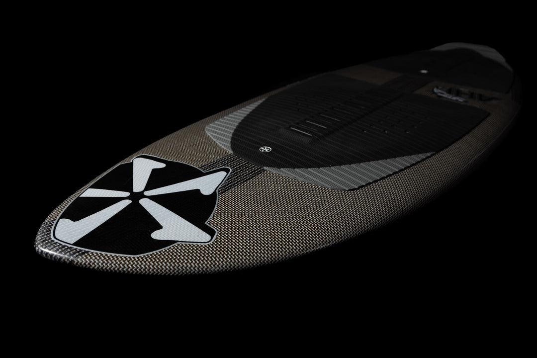 2025 Phase 5 Ahi Stealth surfboard with a carbon fiber finish and a prominent black and white logo on the nose.