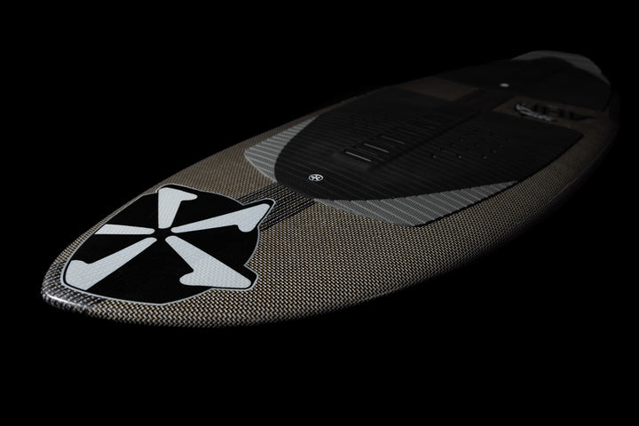 2025 Phase 5 Ahi Stealth surfboard with a carbon fiber finish and a prominent black and white logo on the nose.