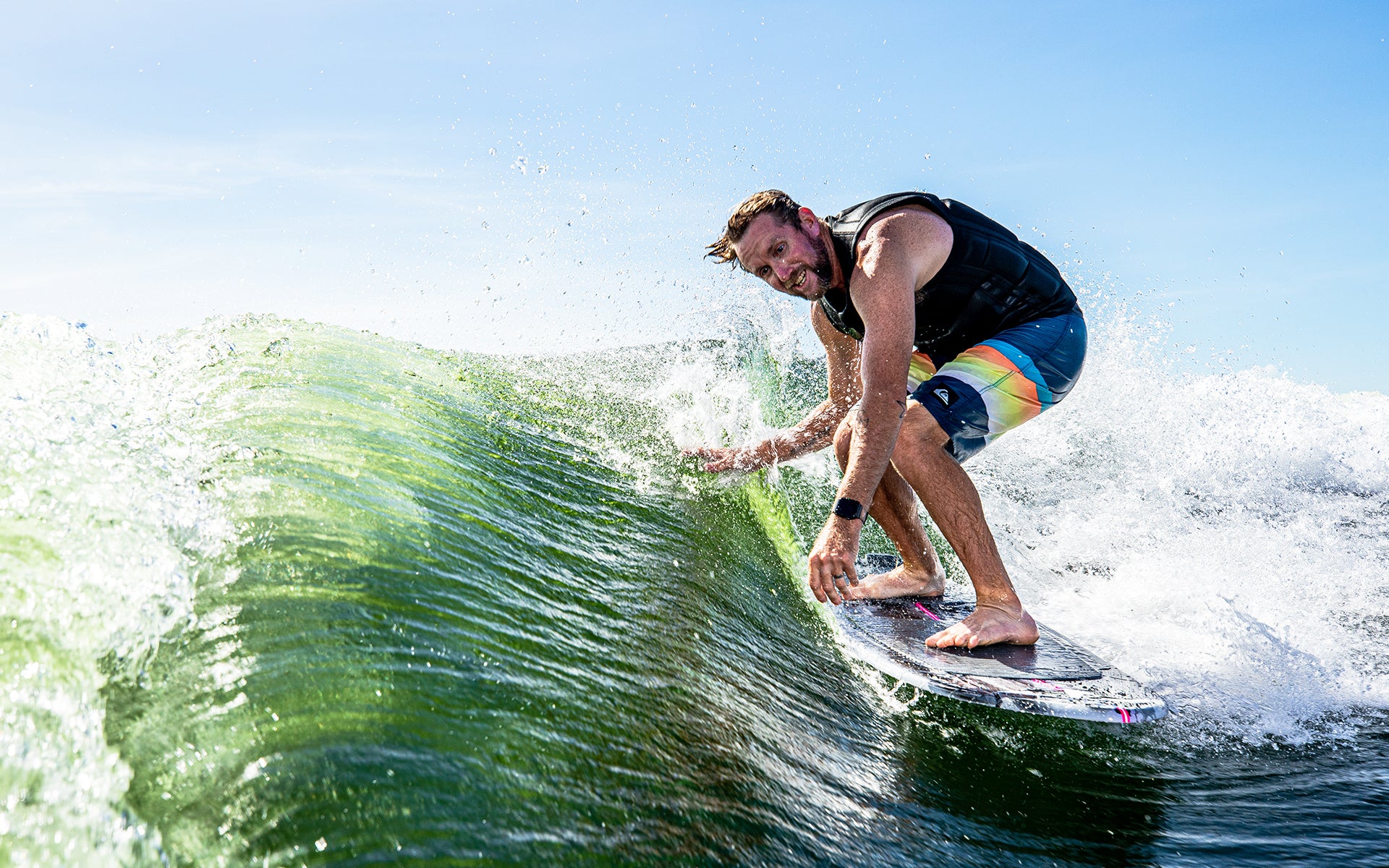 Man riding a wave on a 2025 Phase 5 Oogle skim board, showcasing dynamic movement and water spray.