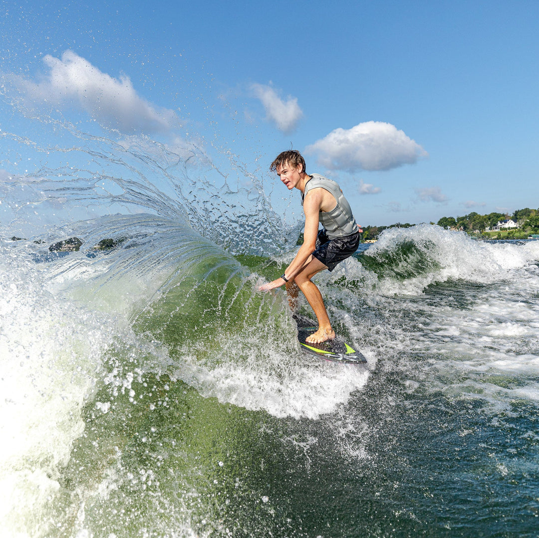 A young man rides the 2026 Phase Five Party Crasher surfboard, carving through a wave with spray flying around him.