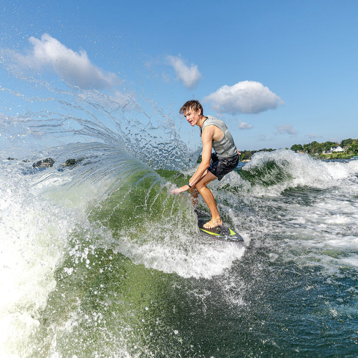 A young man rides the 2026 Phase Five Party Crasher surfboard, carving through a wave with spray flying around him.