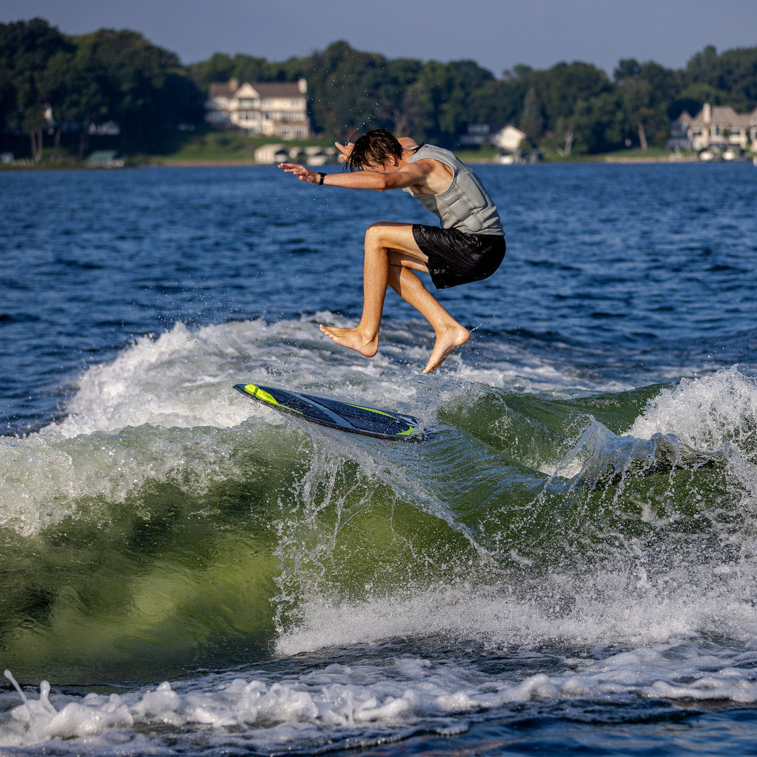 A person jumps off a surfboard while riding a wave on a lake, showcasing the 2026 Phase Five Party Crasher in action.