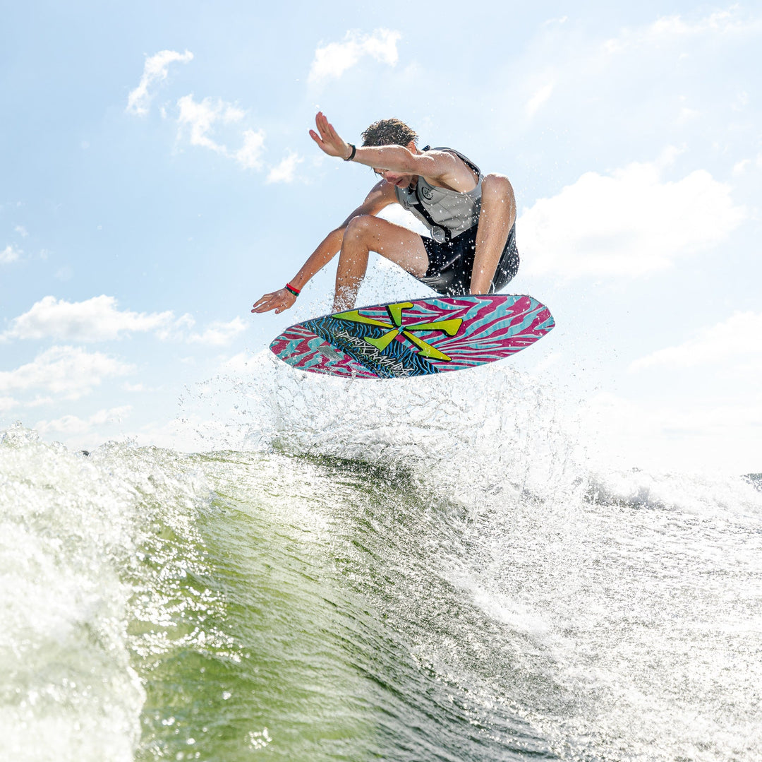 A person performs a jump on a colorful wakeboard over a wave, showcasing the 2026 Phase Five Party Crasher in action.