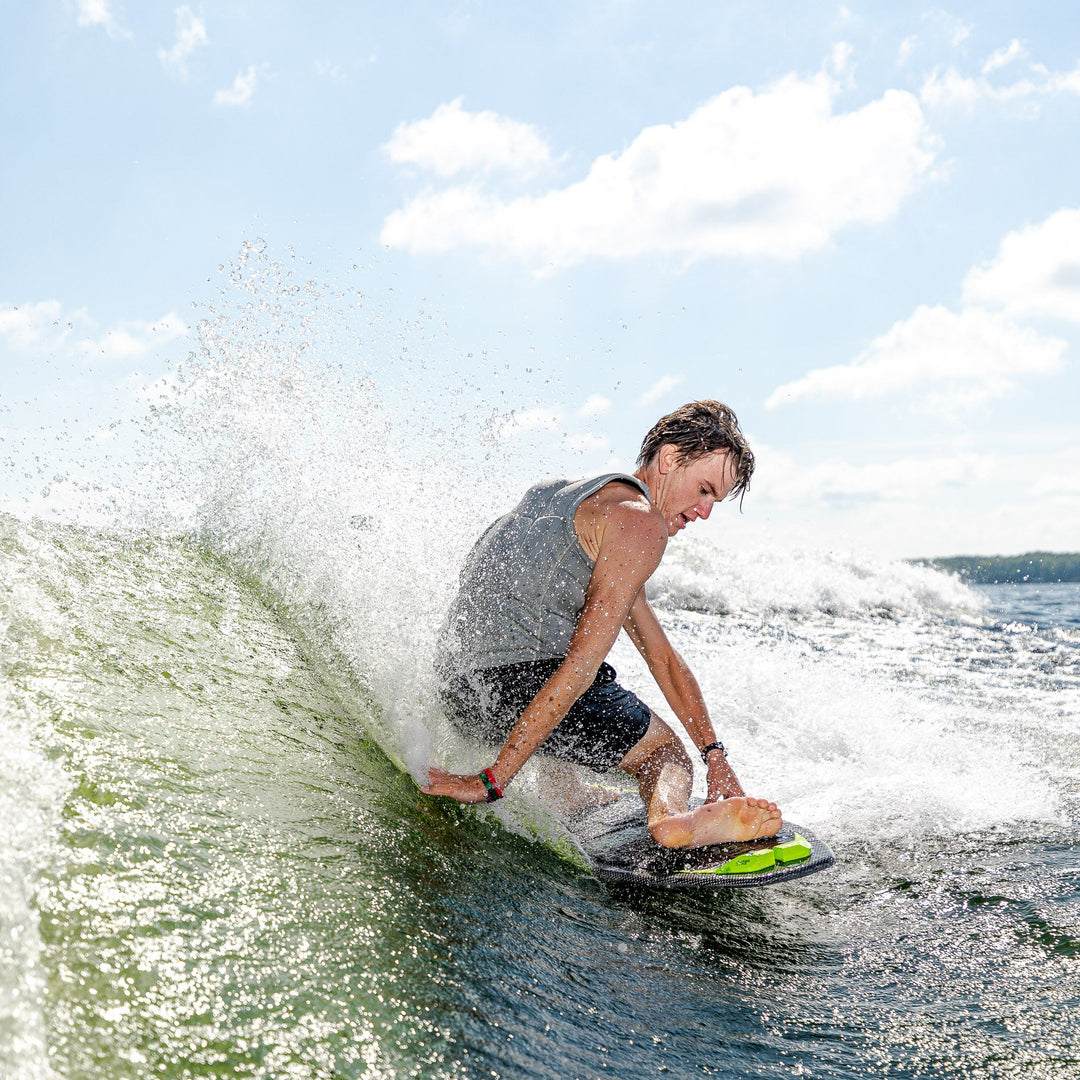 A person riding the 2026 Phase Five Party Crasher wakesurf board, carving through a wave on a sunny day.