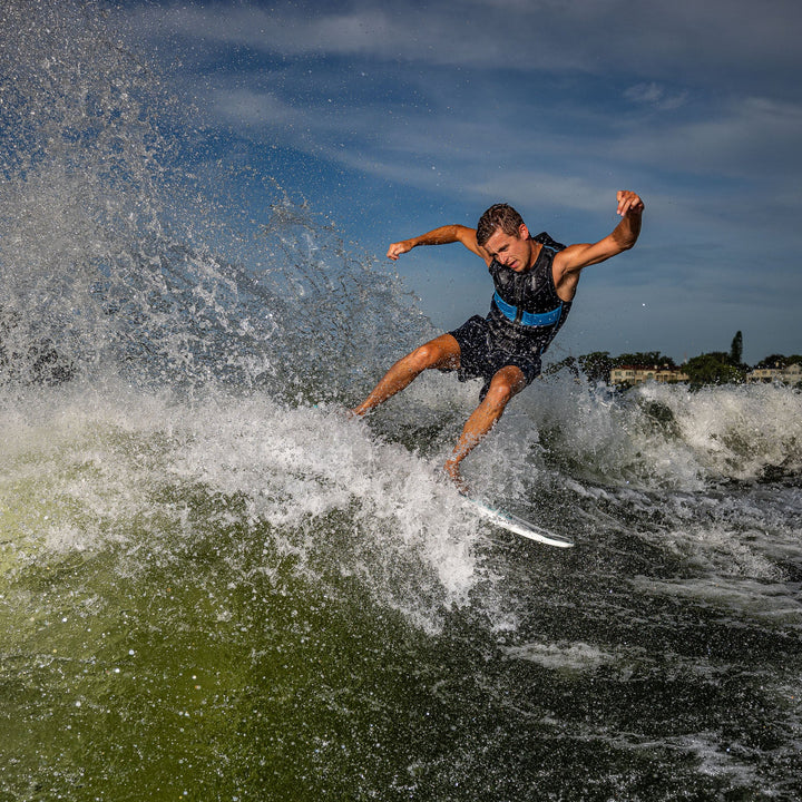 A surfer performing a trick on a 2026 Phase Five Phantom board, creating a spray of water behind him.
