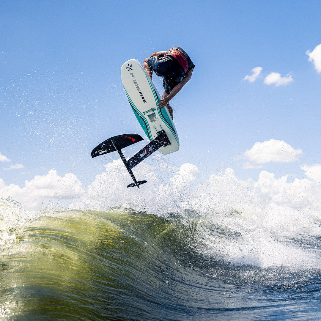 A rider performs a jump on the 2026 Phase Five Phantom Foil above a wave, showcasing its sleek design and performance.