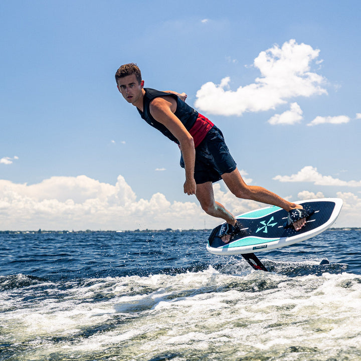 A rider performs a jump on the 2026 Phase Five Phantom Foil, showcasing its sleek design on a sunny water backdrop.