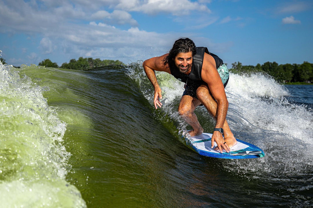 A person rides a wave on a 2025 Phase 5 Prop Skim Board, showcasing dynamic movement and water splashes.