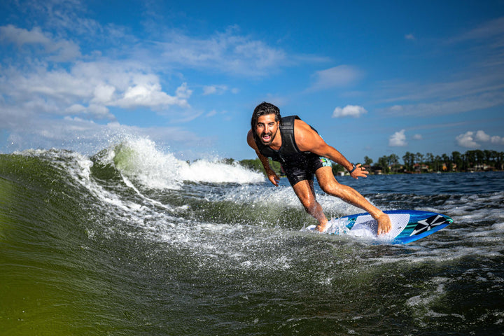 A person riding the 2025 Phase 5 Prop Skim Board on a wave, showcasing dynamic movement and excitement on the water.