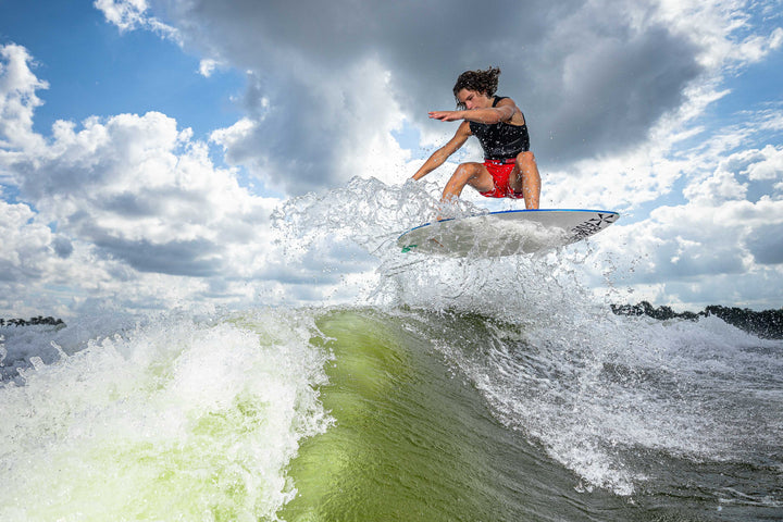 A person performing a trick on a 2025 Phase 5 Prop skim board over a wave, showcasing dynamic water action and skill.