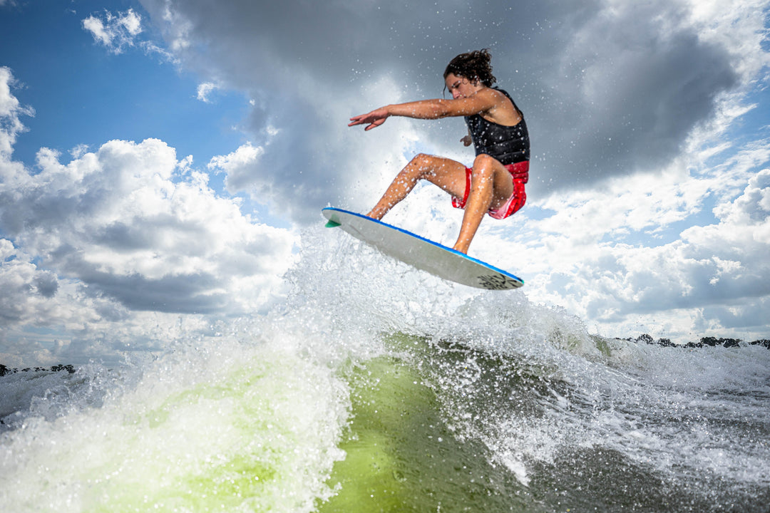 A person performing a jump on a 2025 Phase 5 Prop Skim Board over a wave, showcasing dynamic water sports action.