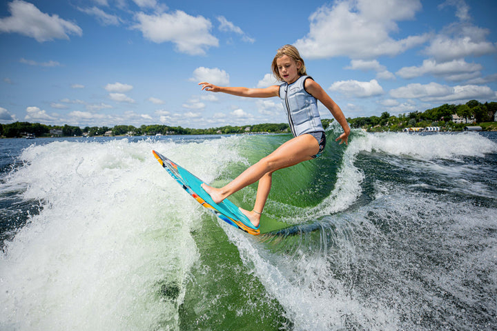 A child rides the 2025 Phase 5 Scamp Skim Board on a wave, showcasing skill and excitement on the water.