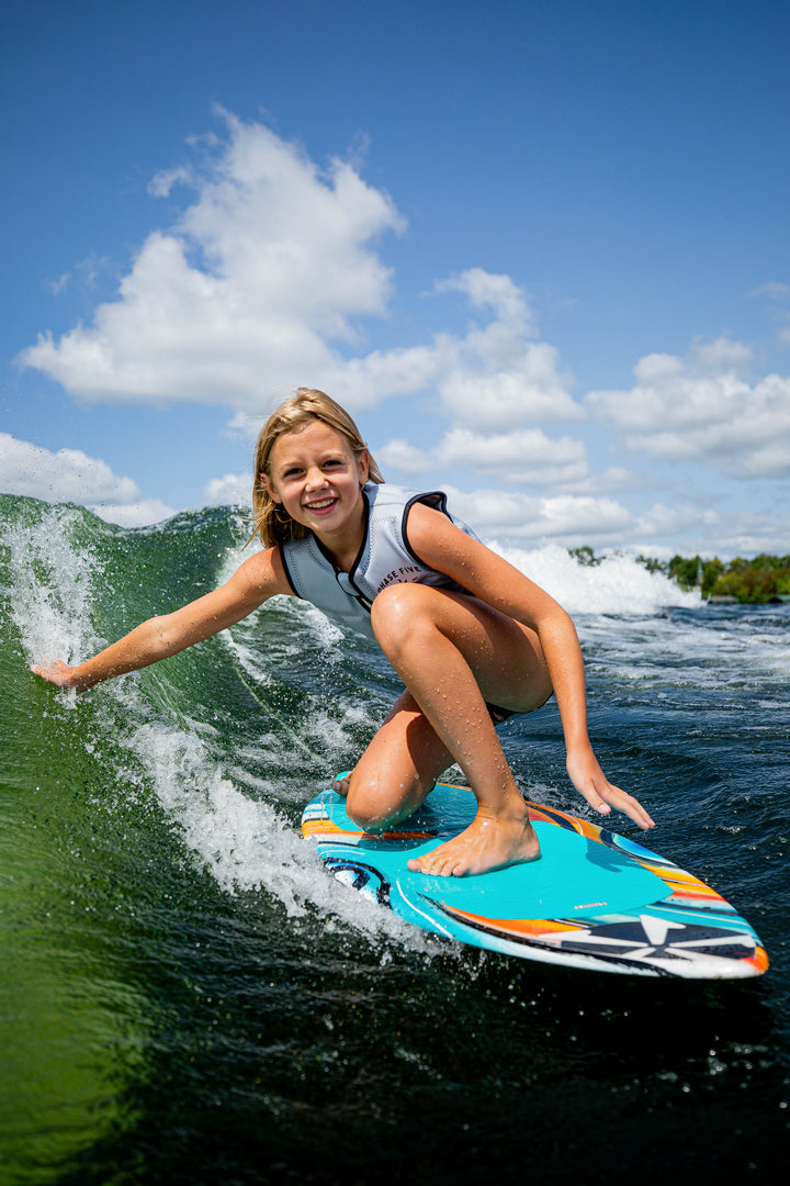 A young girl rides a wave on a 2025 Phase 5 Scamp skim board, showcasing her skills and enjoying the water.