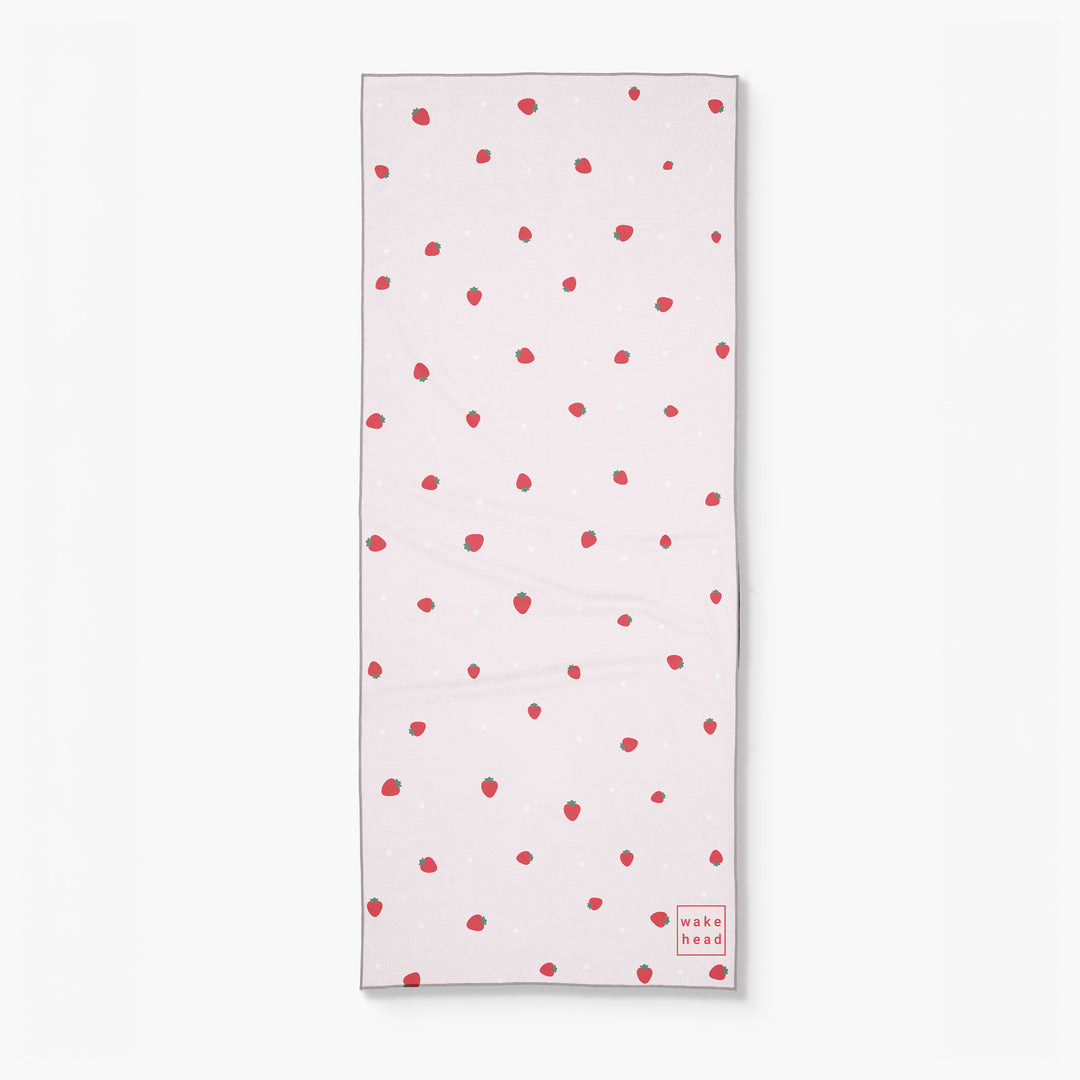 White lake towel with red strawberry pattern and "wake head" logo in red at the bottom right corner.
